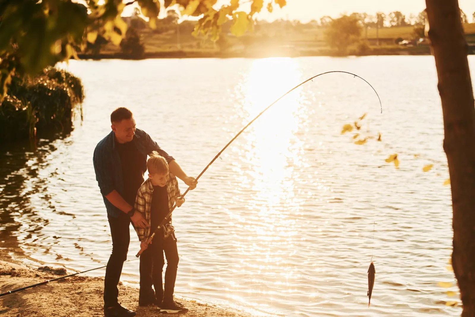 Parent helping a child land a small fish from the shore