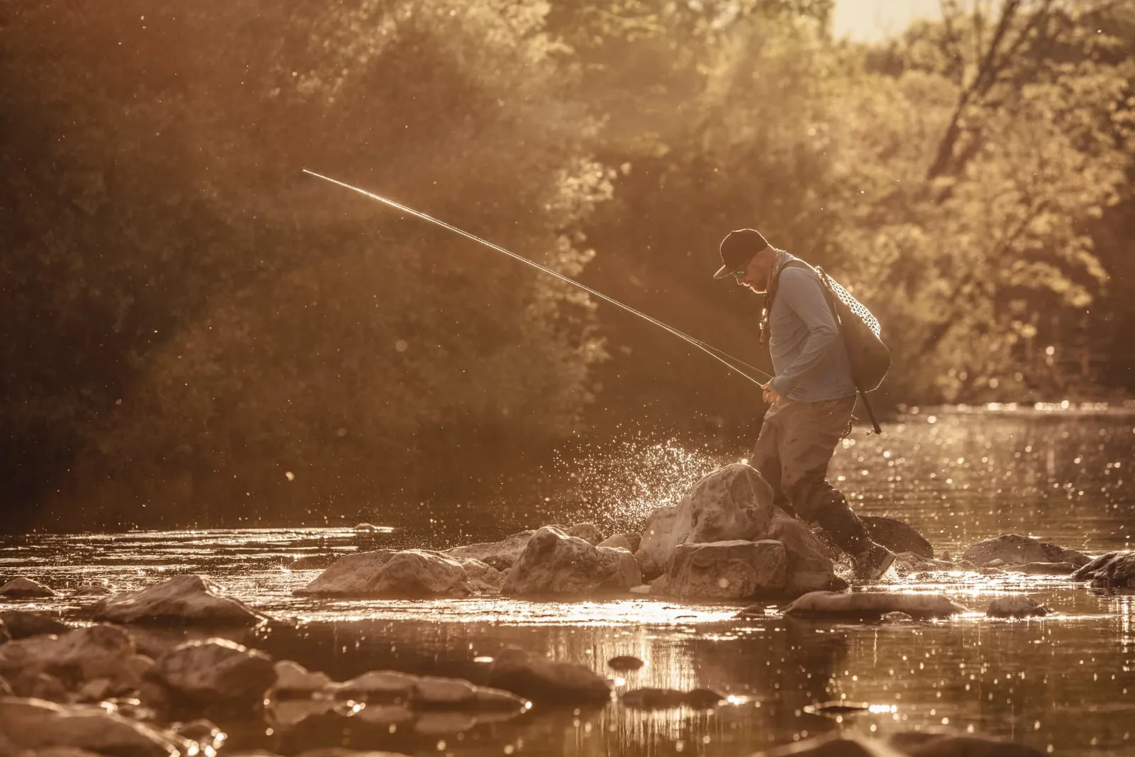 Fly angler stepping across rocks in a sunlit river