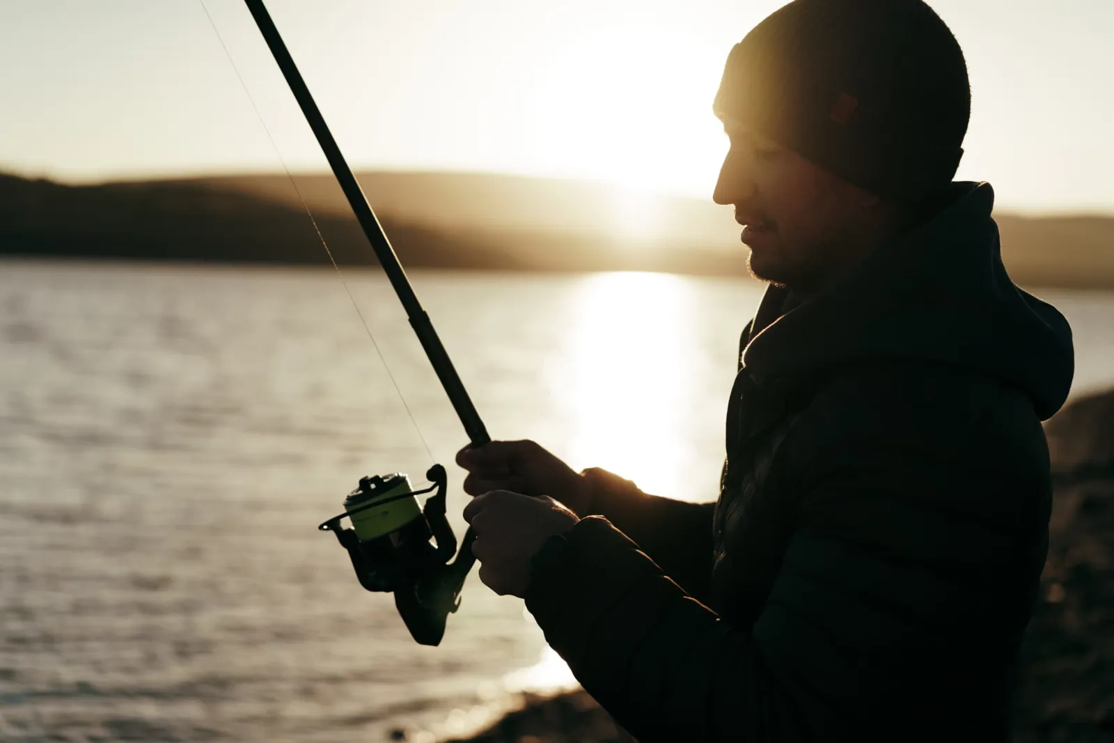 Angler in cold-weather gear working a spinning reel at a lake