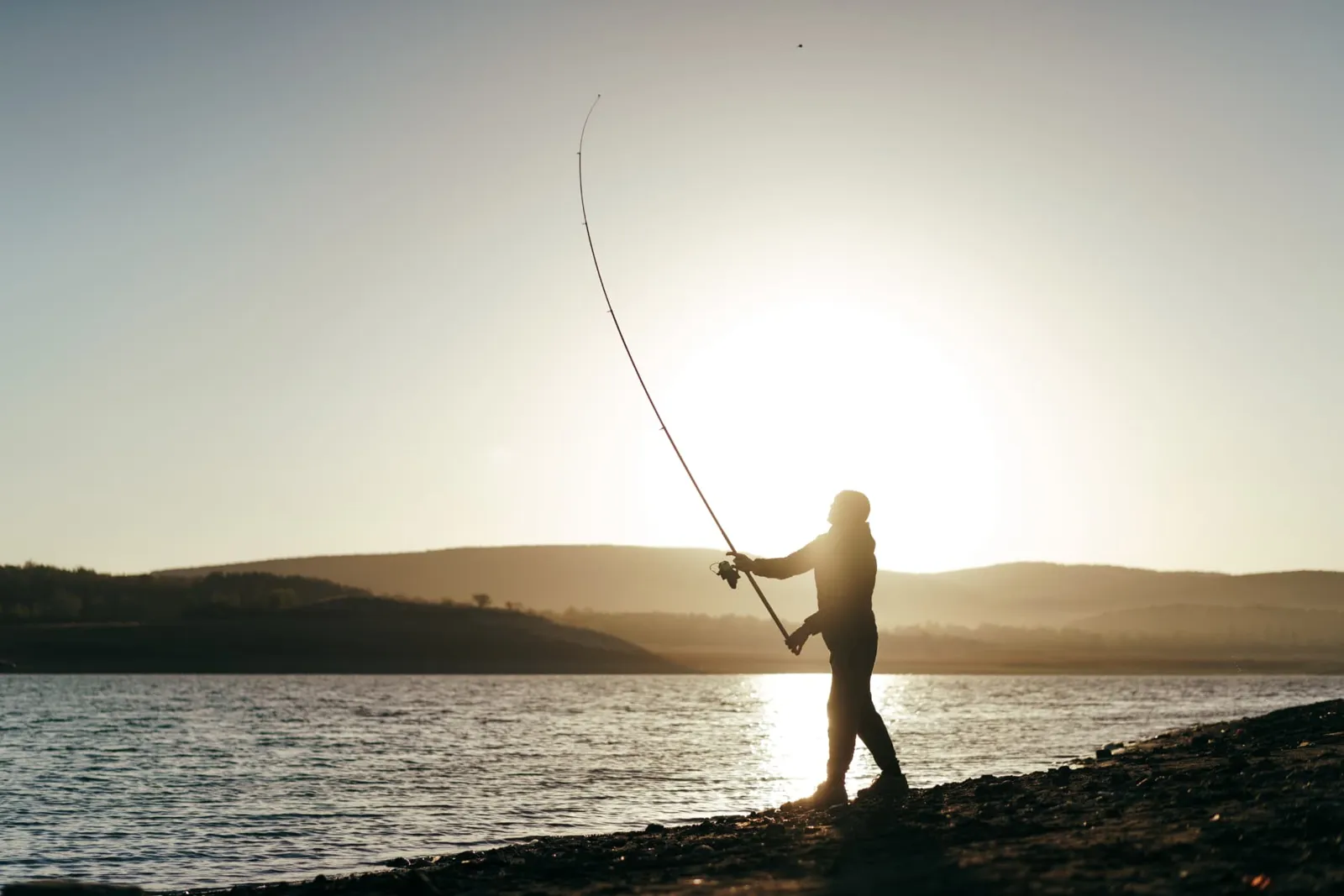 Angler casting from a rocky lakeshore at sunrise